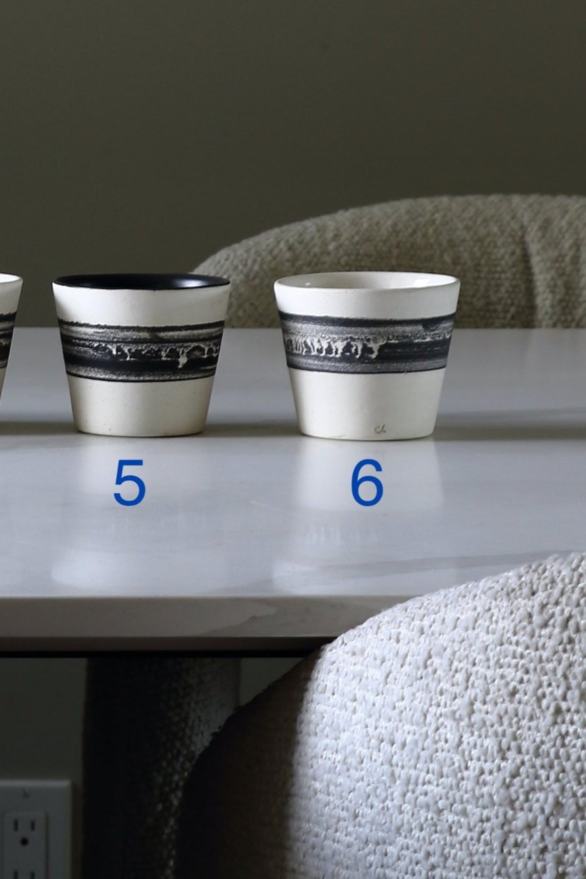 Two white ceramic cups with black bands and a landscape design, labeled with blue numbers 5 and 6 on a tabletop.