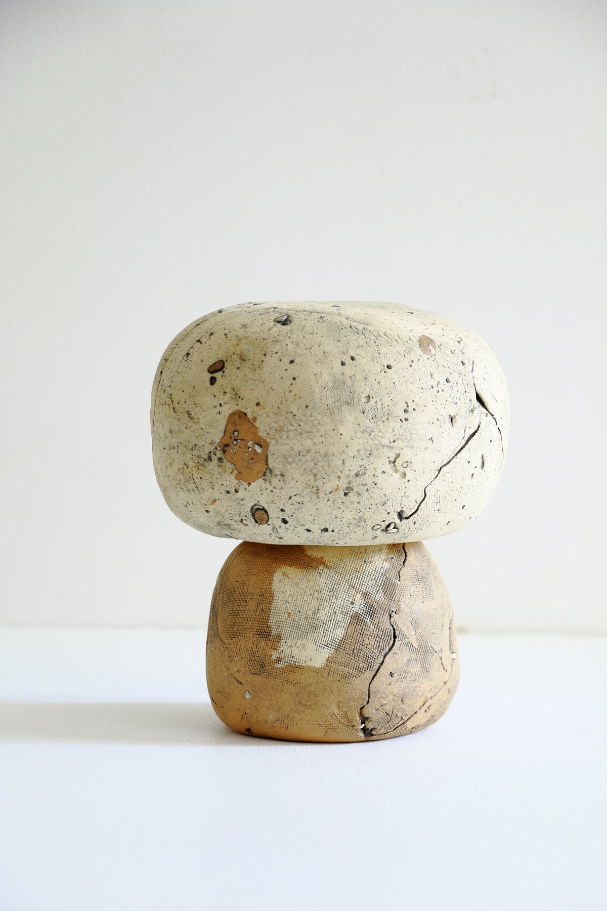 A small sculptural tabletop object made from two stacked natural stones, with a rounded off-white stone on top and a tan-brown stone base, photographed against a plain white studio background.