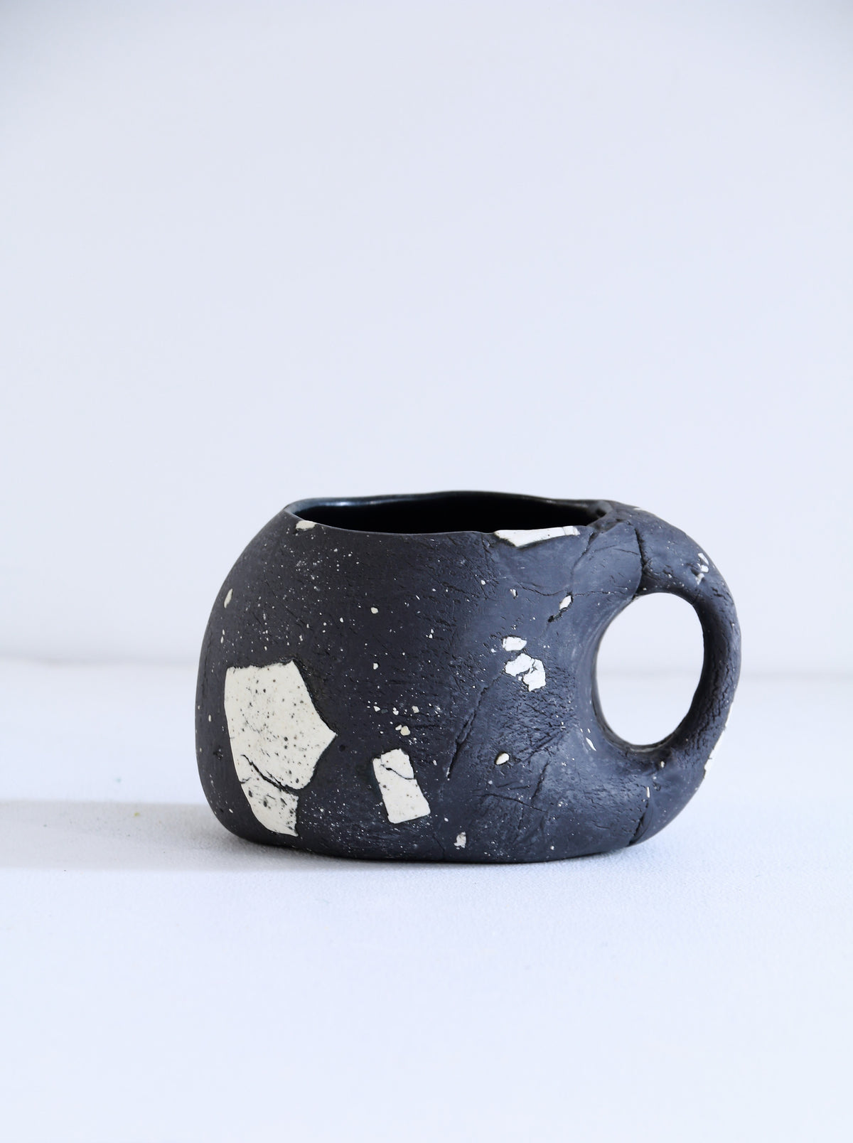 A handmade ceramic mug with a dark charcoal black glaze, featuring white and beige textured inclusions and a loop handle, set against a plain white background.