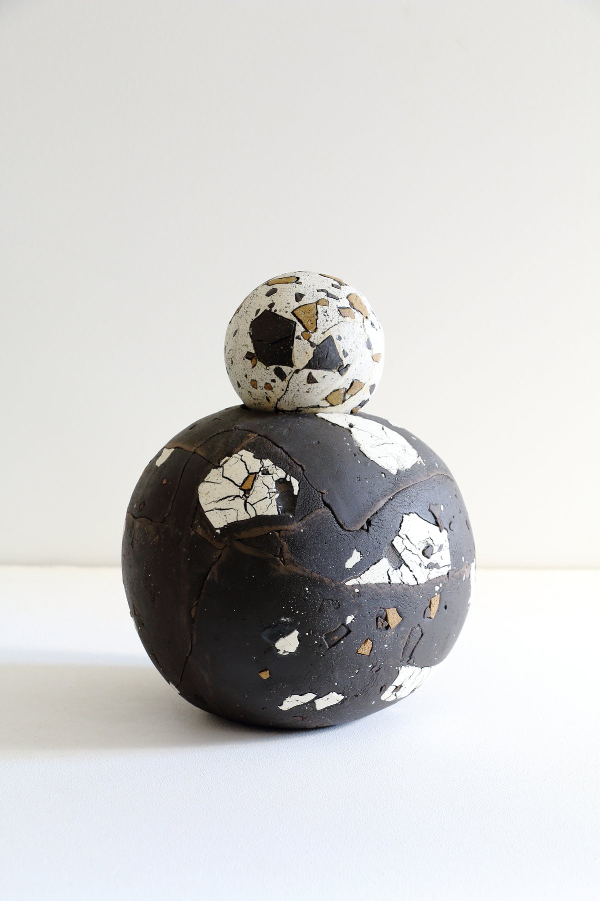 A sculptural decorative object shaped like a soccer ball, featuring a dark charcoal-black lower half with white and gold terrazzo-like chips and a white upper half with black and gold chips, photographed on a clean white background.