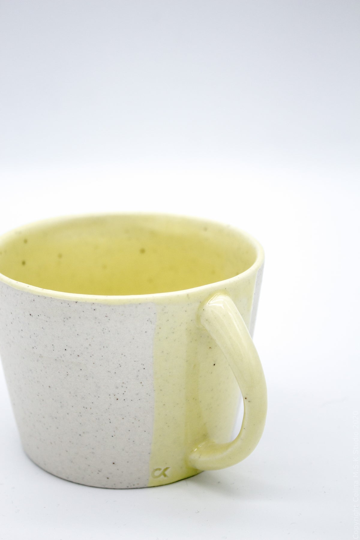 A ceramic mug with a split-color design, featuring a speckled off-white exterior and a pale yellow glazed interior and handle, shown on a white background.