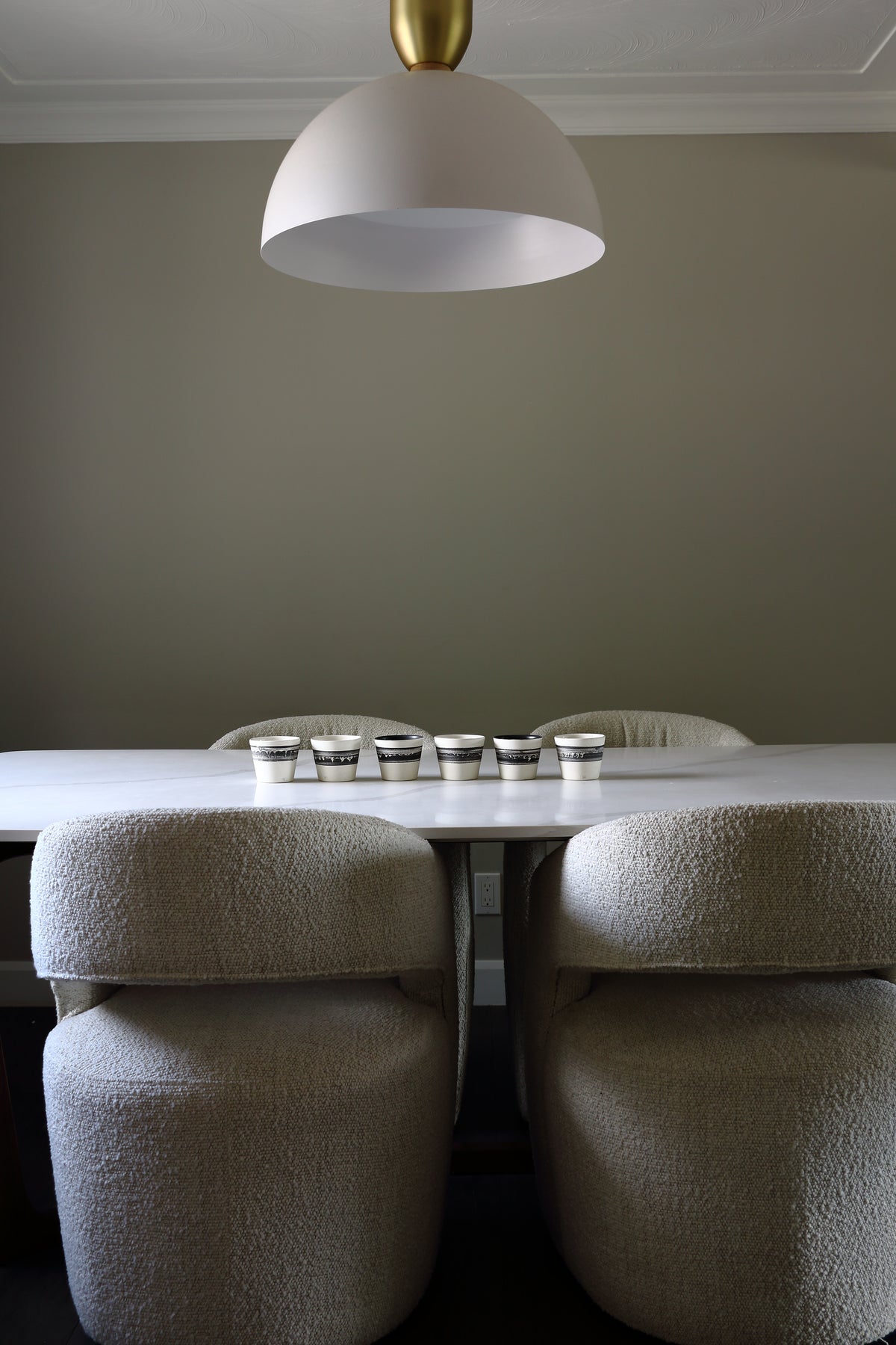 A modern dining room scene featuring a white table, four upholstered bar stools in a textured bouclé fabric, and a large white dome pendant light with a gold finial hanging above.