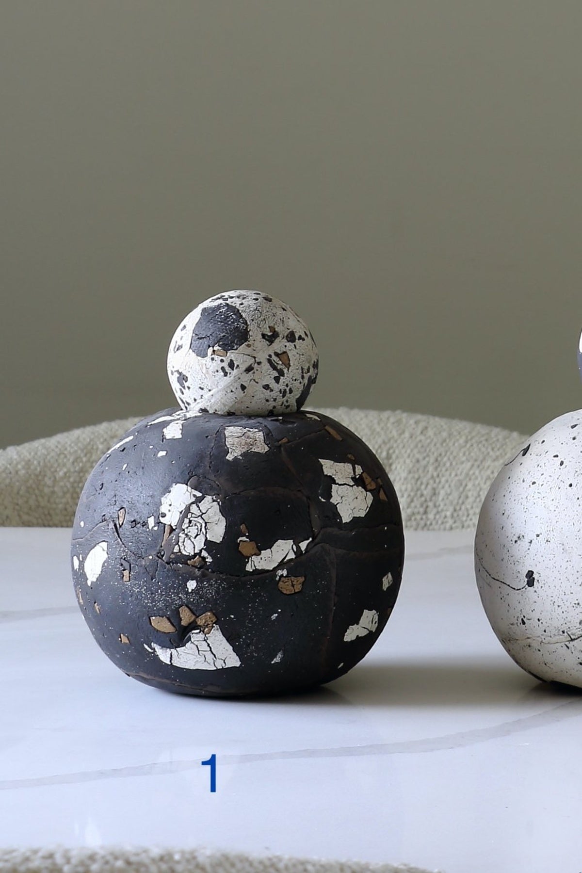 A decorative spherical vessel with a dark charcoal-black body and a smaller matching top, both showing a white and brown terrazzo-like speckled pattern. The vessel sits on a light surface with a neutral background.