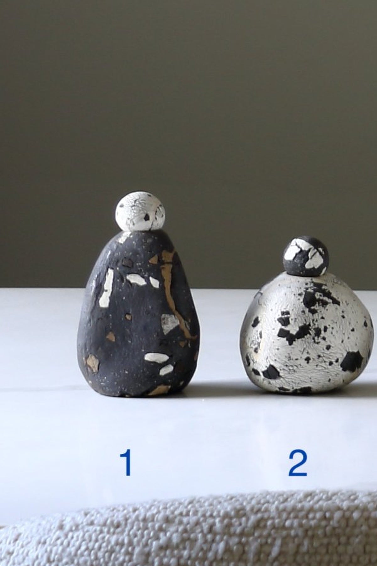 Two small decorative stone figurines with a speckled finish, labeled 1 and 2, displayed on a white surface against a dark gray background.