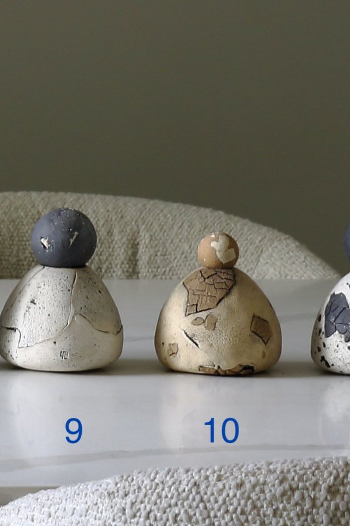 Two small decorative ceramic figurines displayed on a white surface against a neutral background. The left figurine is off-white with a dark gray top and visible crackle glaze details.