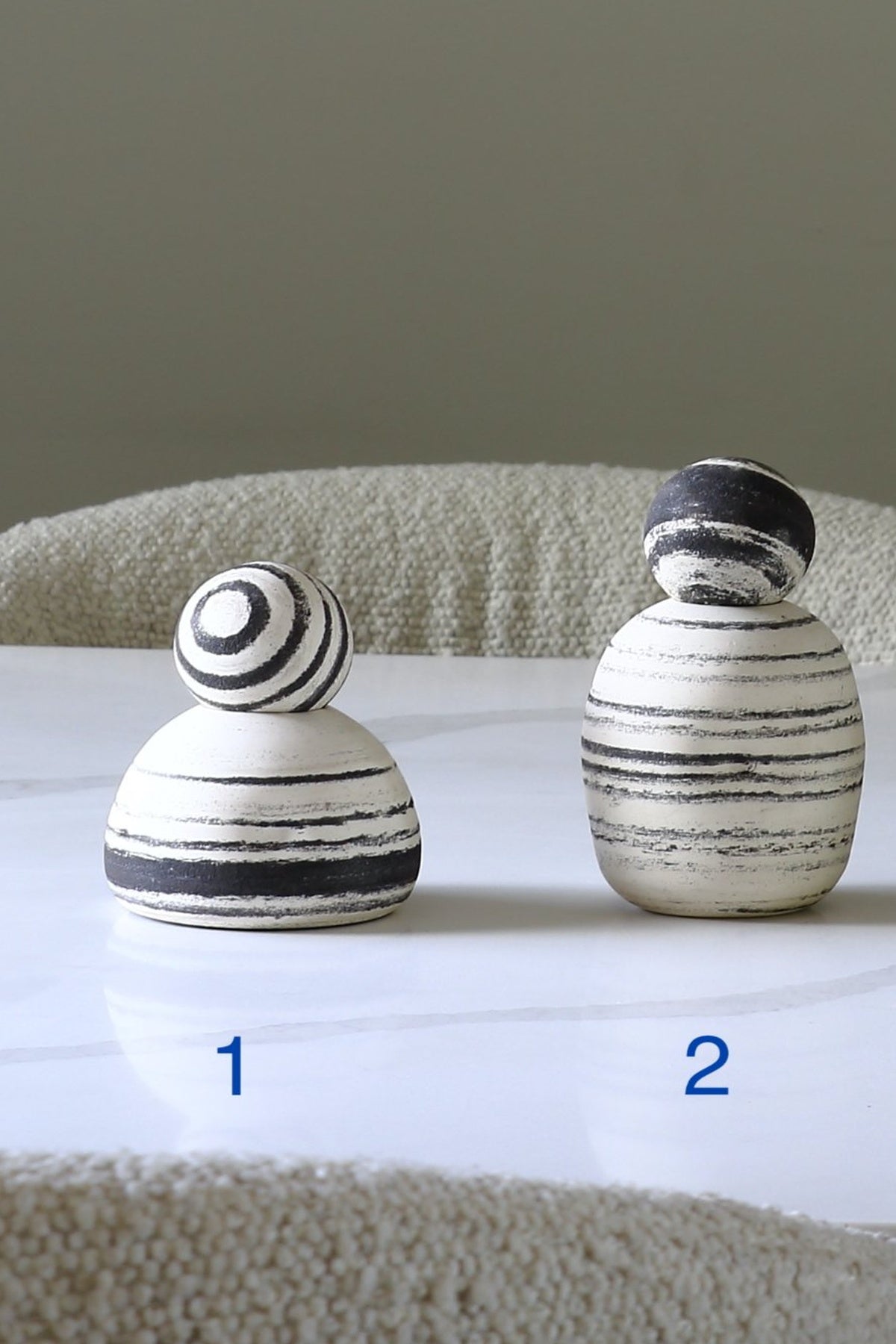 Two small decorative ceramic pinnies with black and white striped patterns, labeled 1 and 2, sitting on a white marble surface with a neutral background.
