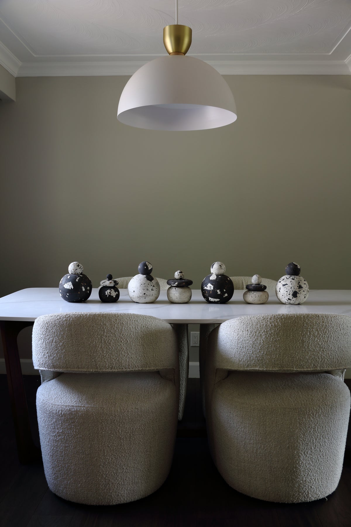 A dining area scene with a white table, two upholstered chairs, a white pendant light with a gold top, and a row of small black-and-white decorative bird figurines on the tabletop.