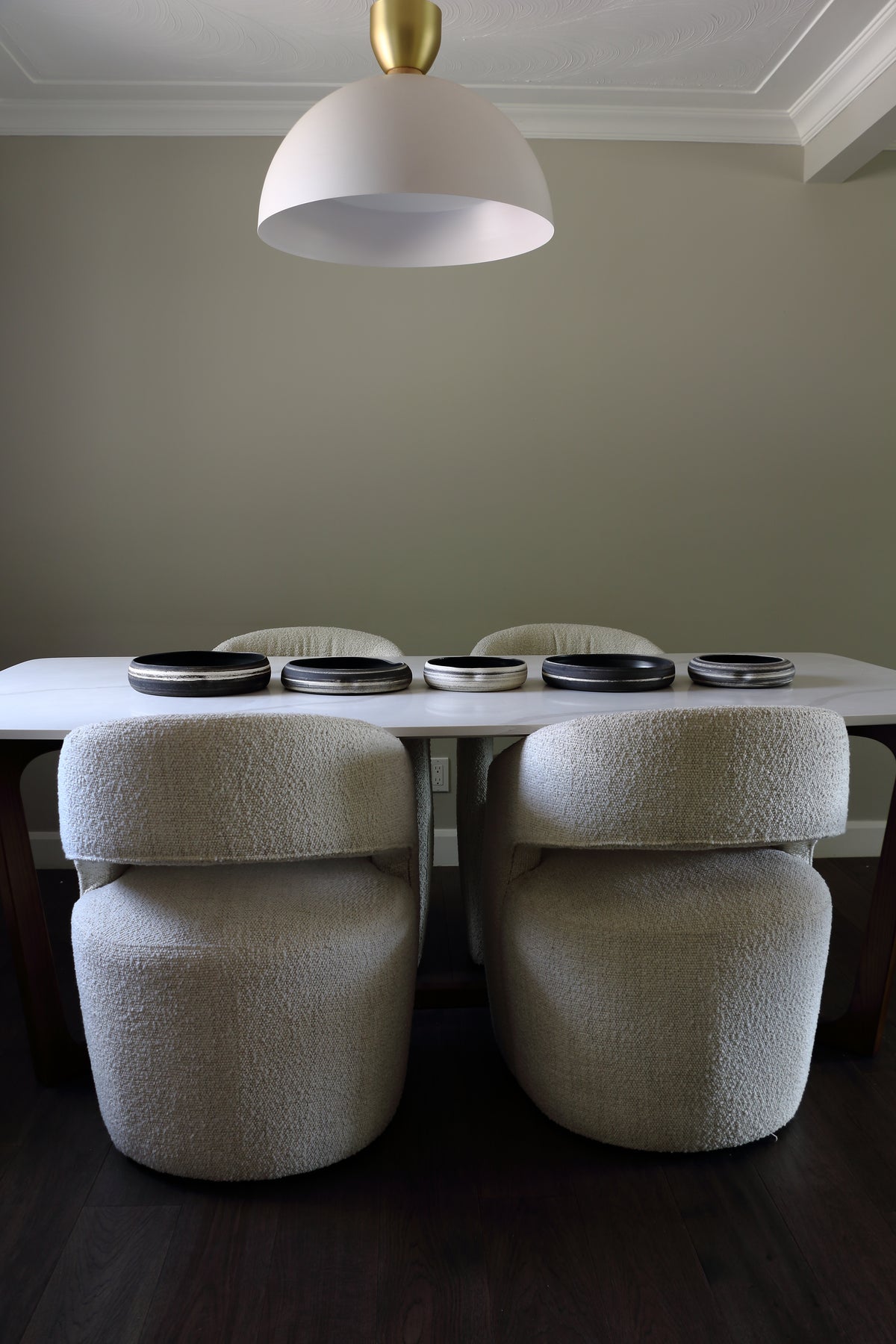 A dining table with four upholstered chairs in a textured cream bouclé fabric, set under a white dome pendant light with a gold finial in a minimalist dining room.
