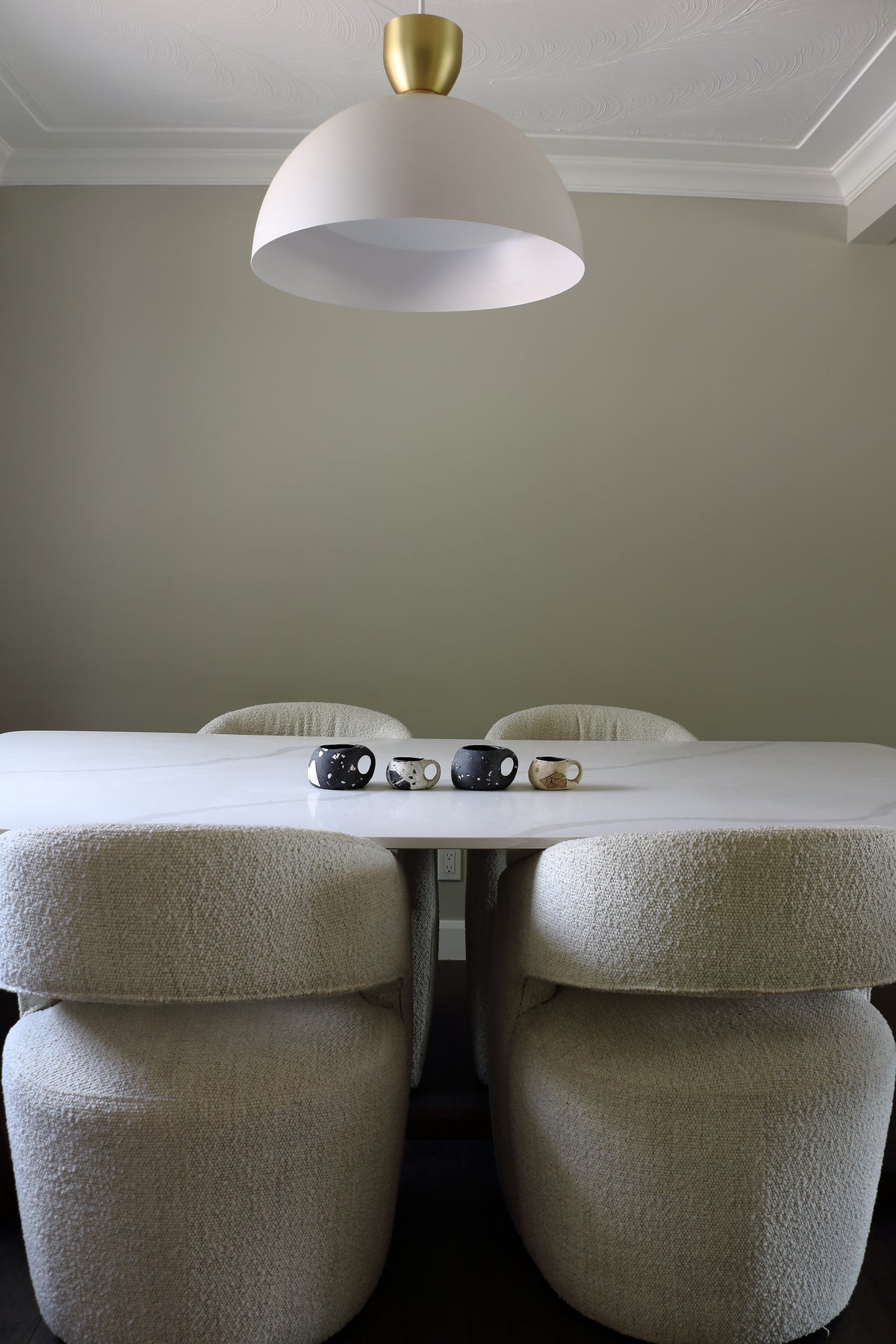 A modern dining room scene featuring a white table and four upholstered chairs in a textured cream bouclé fabric, with a large white dome pendant light hanging above.
