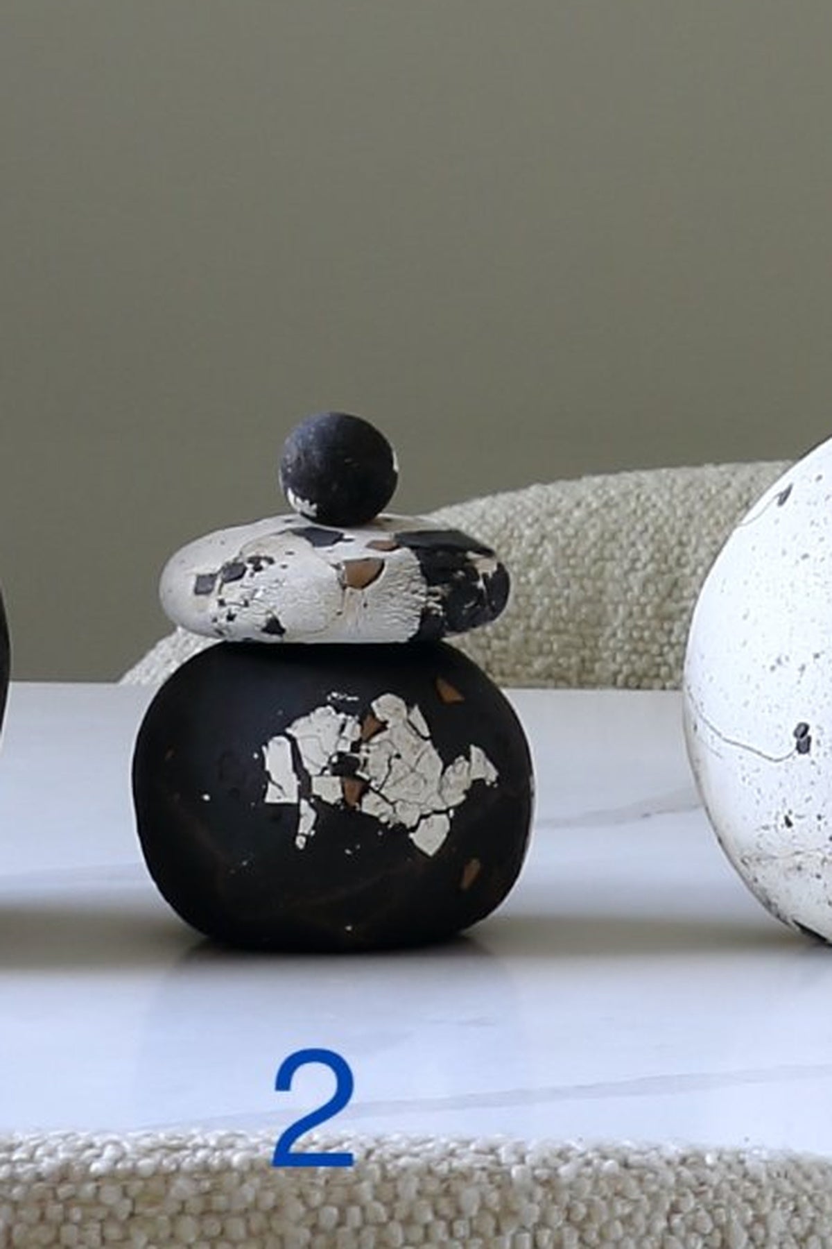 A small decorative lidded container or vase with a rounded black body and a stacked lid in black, white, and brown marbled stone, shown on a tabletop with a textured neutral background.