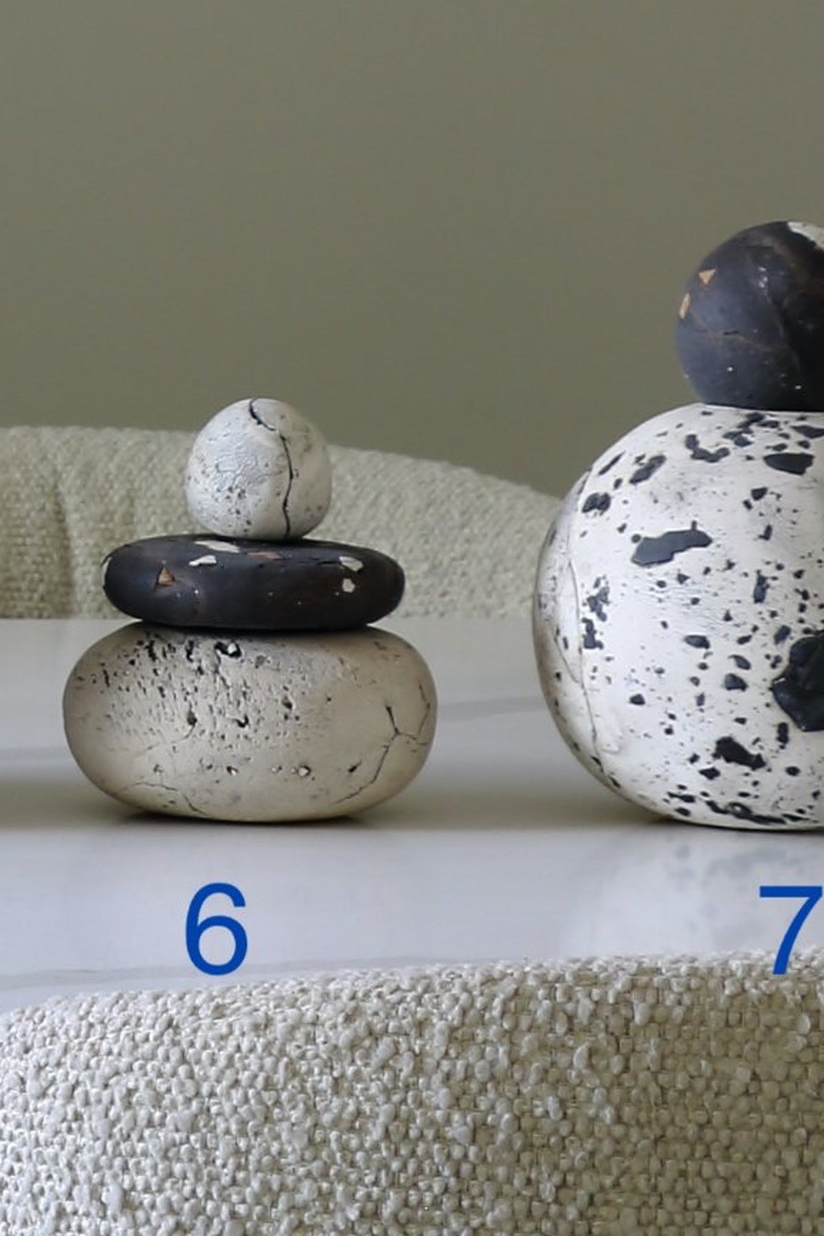 Two decorative stacked stone vessels on a white surface against a beige wall. The left vessel is a small stack of three stones in off-white and charcoal.