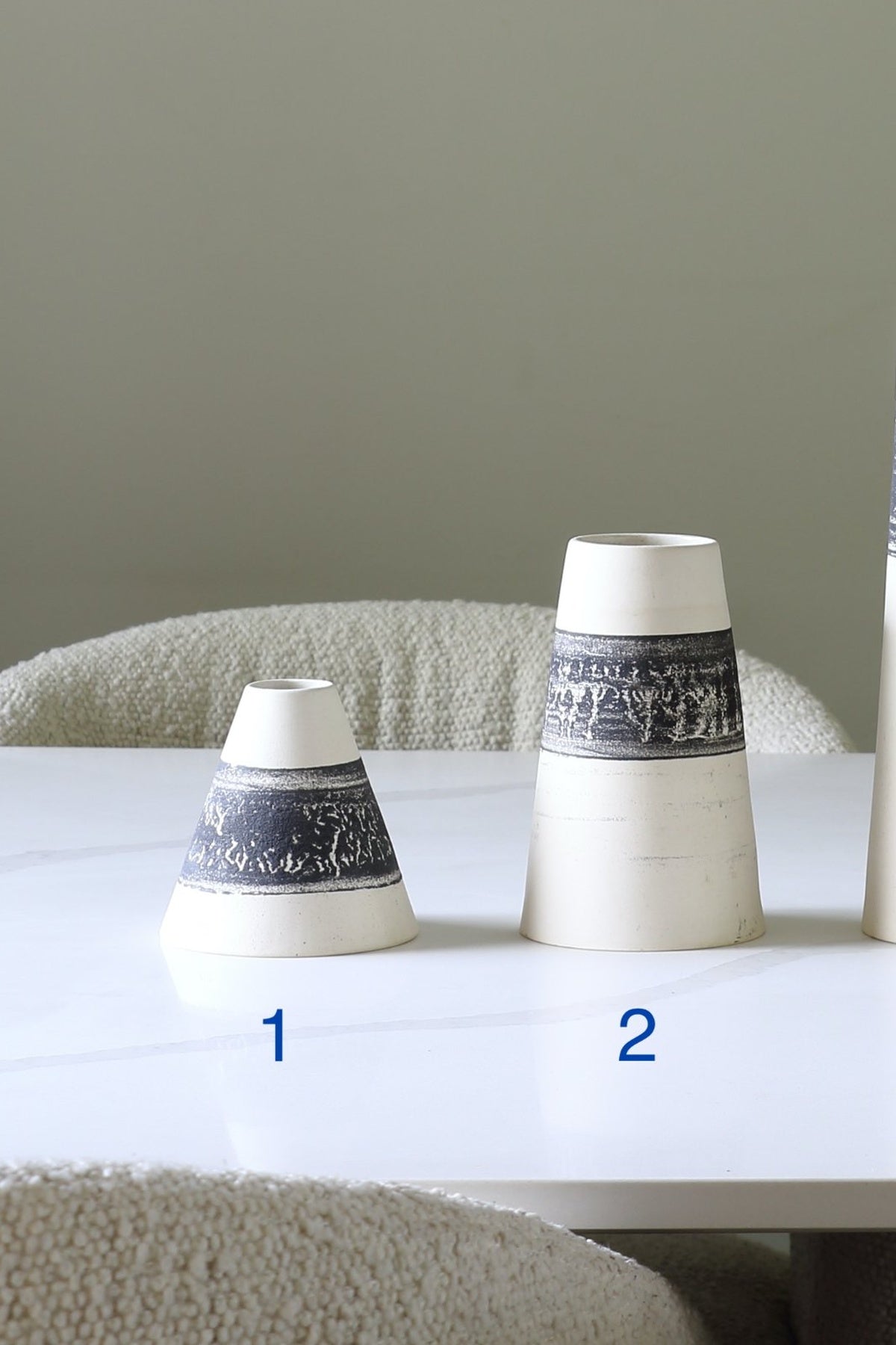 Two small tapered ceramic vases with a dark blue and white landscape band, displayed on a white table with blue numbers 1 and 2 indicating sizes.